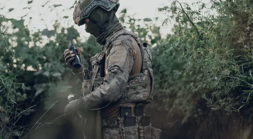 Зв’язківець у траншеї передає повідомлення портативною радіостанцією.